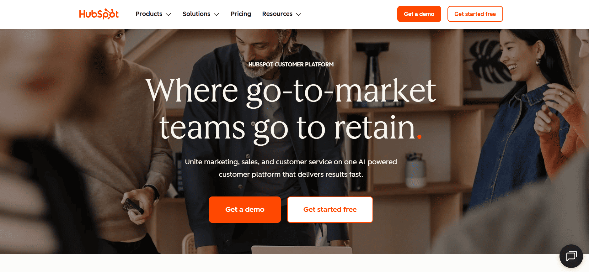 HubSpot webpage with team collaborating in a modern office, headline "Where go-to-market teams go to retain," demo and free start options.