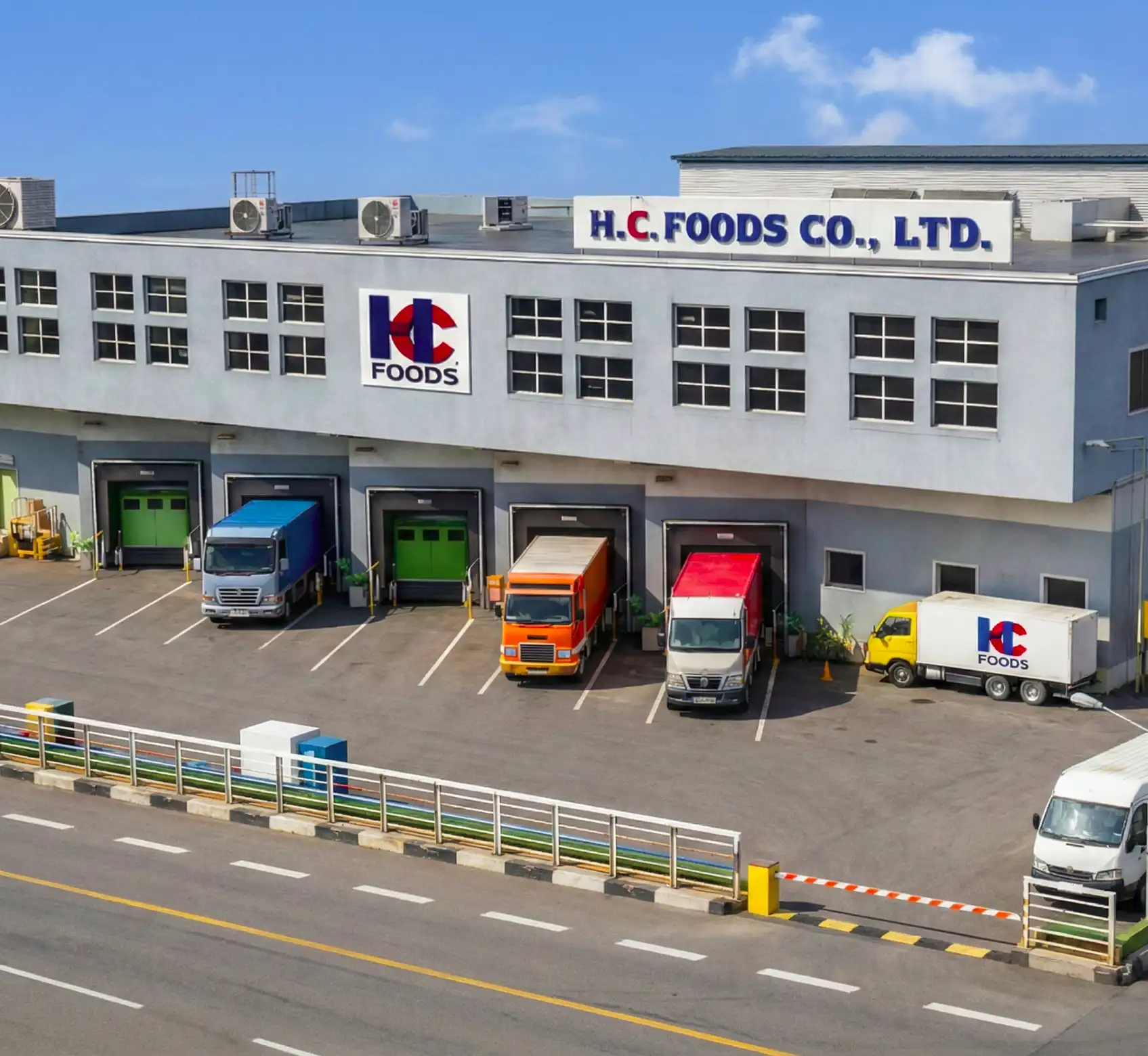 H.C. FOODS CO., LTD food distribution center with five trucks at loading bays and a white truck driving past the gray building.